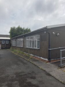 The outside of the cadet hut, brown and weathered, before works started.