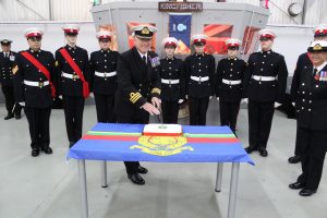 Commander Mills cutting the cake with cadets stood round smartly.